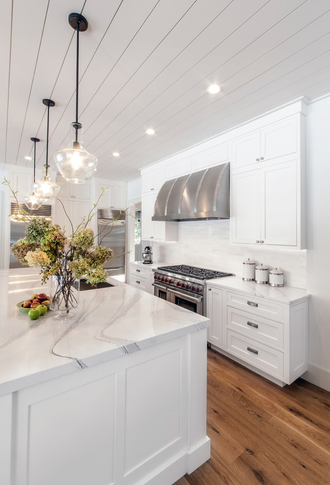 Example of a large transitional l-shaped light wood floor and beige floor open concept kitchen design in New York with an undermount sink, flat-panel cabinets, white cabinets, quartzite countertops, white backsplash, porcelain backsplash, stainless steel appliances and an island