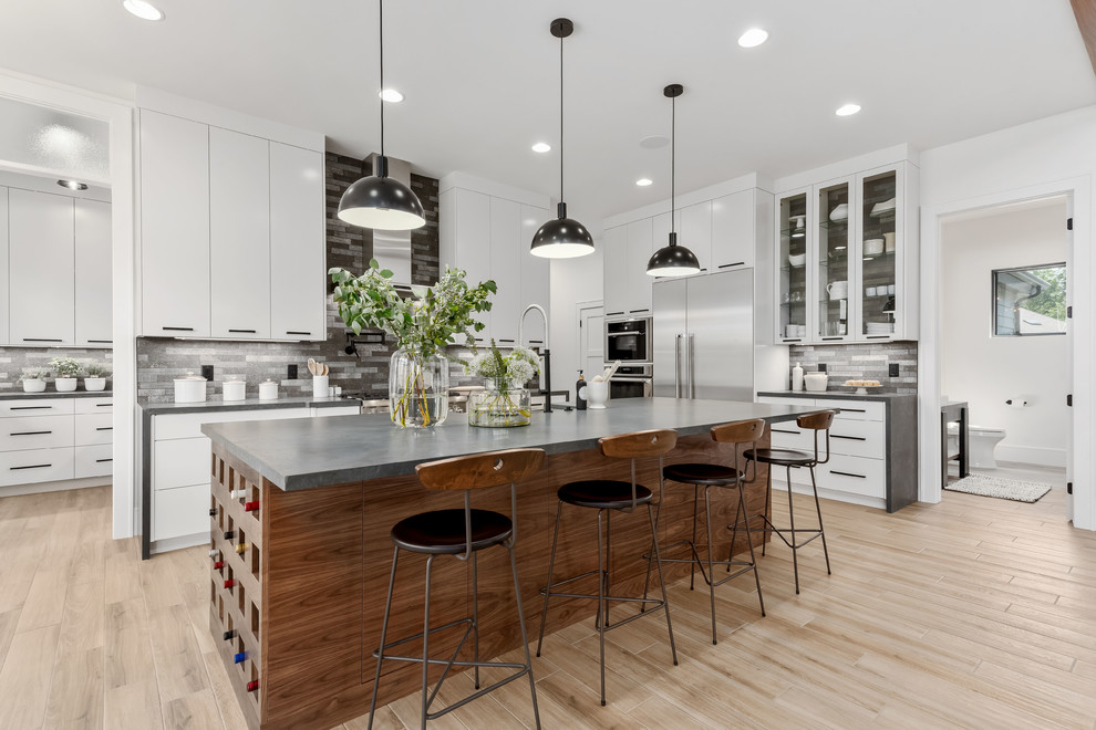 Inspiration for a large contemporary l-shaped porcelain tile and beige floor eat-in kitchen remodel in Salt Lake City with a farmhouse sink, flat-panel cabinets, white cabinets, quartzite countertops, gray backsplash, stone tile backsplash, stainless steel appliances, an island and gray countertops