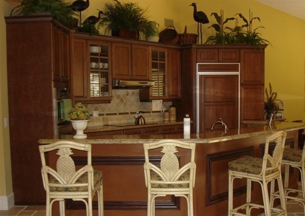 Idéer för att renovera ett litet tropiskt kök och matrum, med en undermonterad diskho, luckor med glaspanel, gula skåp, granitbänkskiva, beige stänkskydd, stänkskydd i stenkakel, integrerade vitvaror, travertin golv och en halv köksö