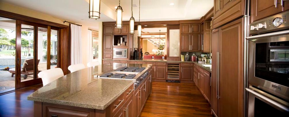 Bild på ett tropiskt l-kök, med luckor med upphöjd panel, skåp i mellenmörkt trä, granitbänkskiva, rostfria vitvaror, mellanmörkt trägolv och en köksö