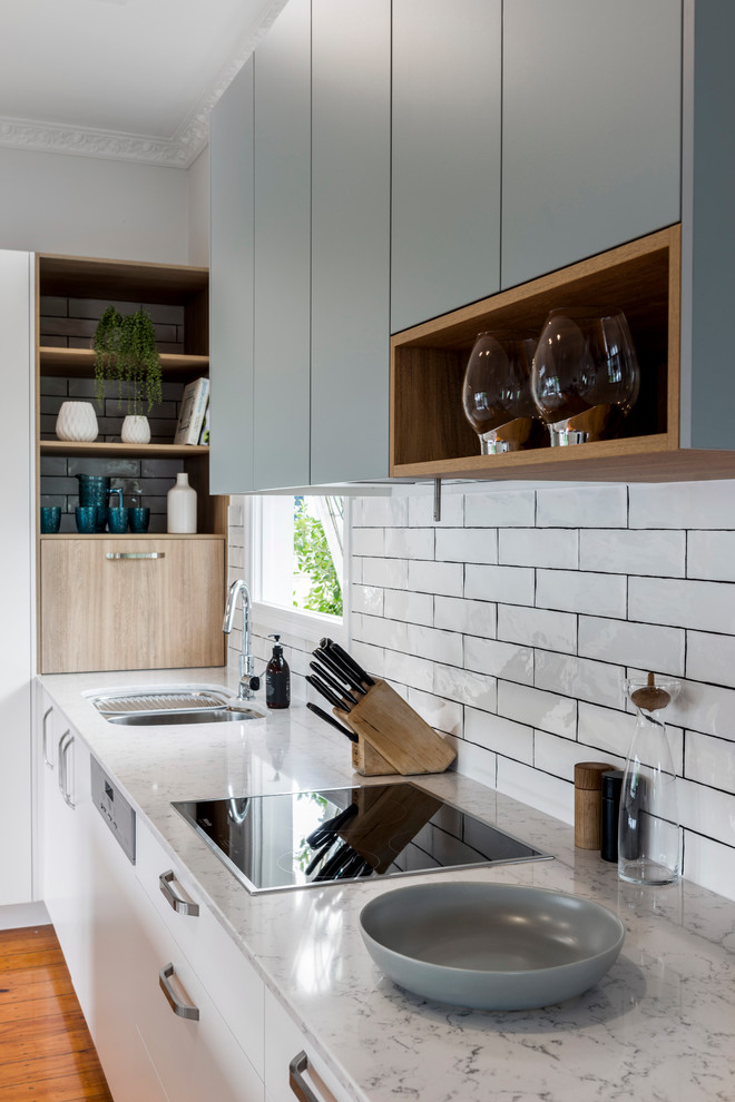 Inspiration for a medium sized contemporary l-shaped open plan kitchen in Brisbane with a submerged sink, flat-panel cabinets, white cabinets, engineered stone countertops, white splashback, ceramic splashback, white appliances, medium hardwood flooring, an island and brown floors.