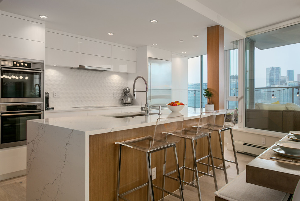 Open concept kitchen - mid-sized contemporary l-shaped light wood floor and beige floor open concept kitchen idea in Vancouver with an undermount sink, flat-panel cabinets, white cabinets, marble countertops, white backsplash, ceramic backsplash, stainless steel appliances and an island