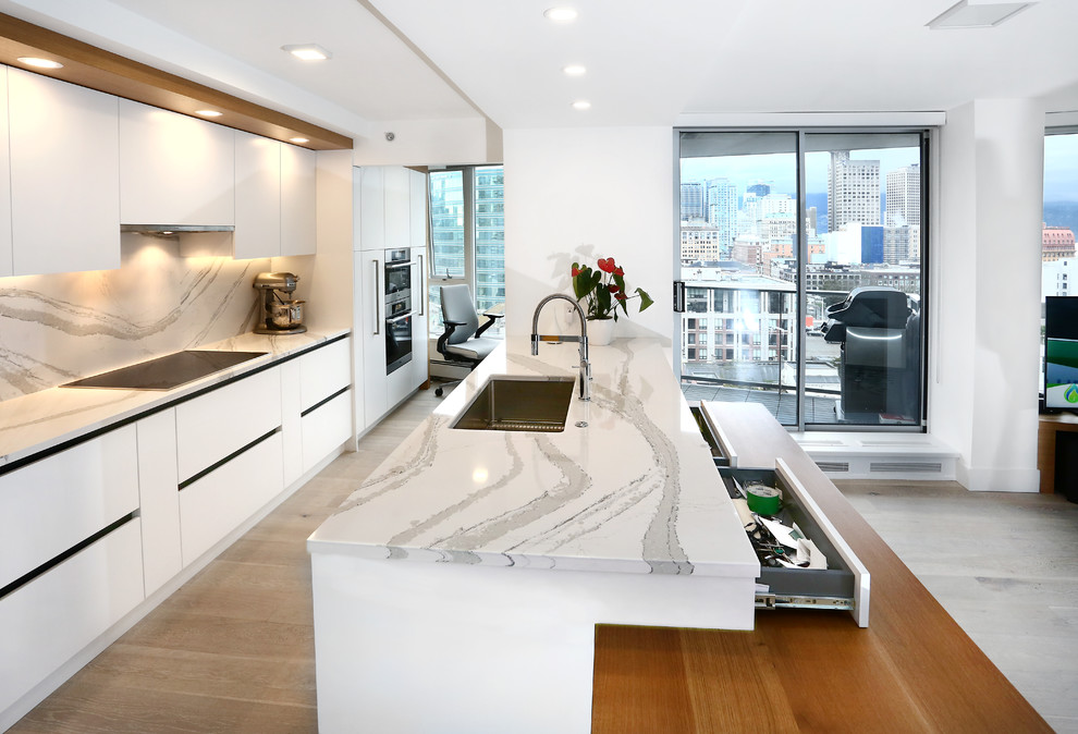 Photo of a small contemporary galley kitchen/diner in Vancouver with a built-in sink, flat-panel cabinets, white cabinets, granite worktops, white splashback, porcelain splashback, stainless steel appliances, light hardwood flooring, an island and grey floors.