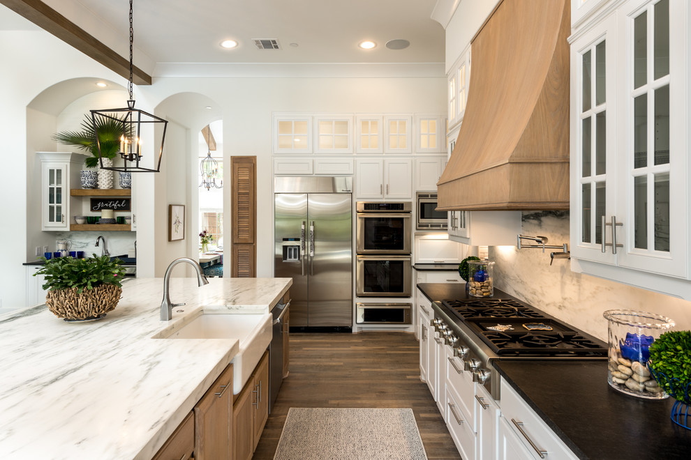 Mid-sized transitional single-wall medium tone wood floor and brown floor open concept kitchen photo in Dallas with a farmhouse sink, shaker cabinets, white cabinets, quartz countertops, white backsplash, marble backsplash, stainless steel appliances and an island