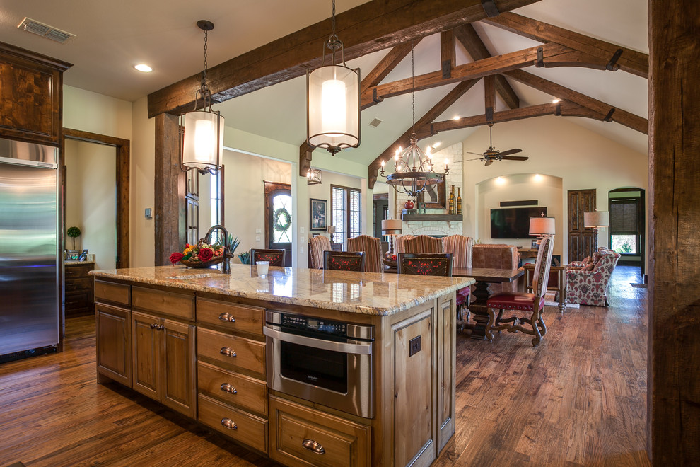 Large mountain style u-shaped medium tone wood floor open concept kitchen photo in Dallas with an undermount sink, louvered cabinets, dark wood cabinets, granite countertops, beige backsplash, stone tile backsplash, stainless steel appliances and an island