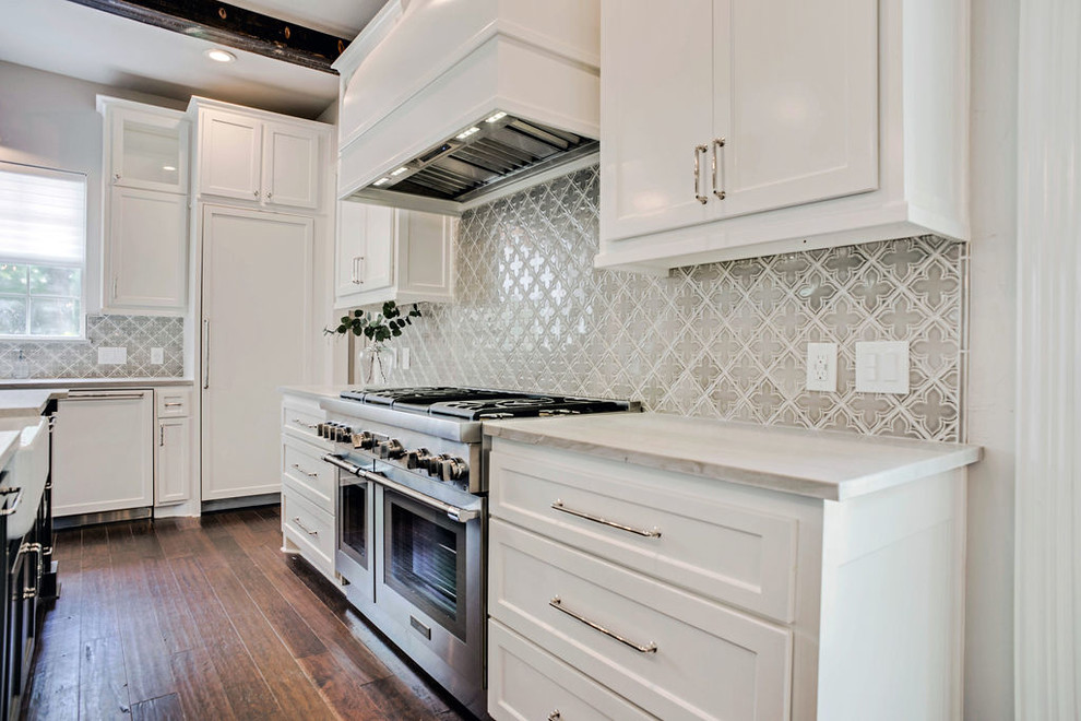 Inredning av ett klassiskt mellanstort vit vitt kök, med en rustik diskho, luckor med infälld panel, vita skåp, bänkskiva i kvartsit, grått stänkskydd, stänkskydd i keramik, integrerade vitvaror, mellanmörkt trägolv, en köksö och brunt golv