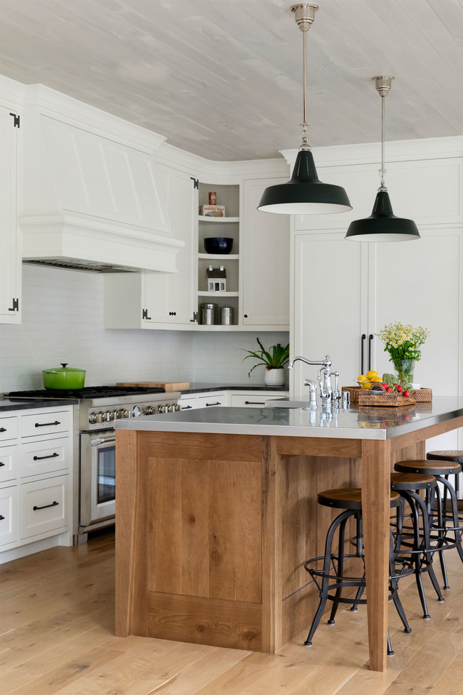 Inspiration for a cottage l-shaped light wood floor and beige floor kitchen remodel in Minneapolis with a farmhouse sink, shaker cabinets, white cabinets, white backsplash, stainless steel appliances, an island and black countertops