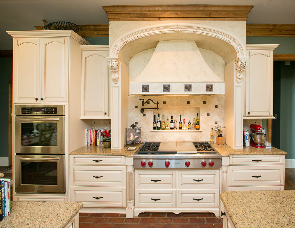 Ejemplo de cocina tradicional con armarios con paneles con relieve, puertas de armario beige, salpicadero beige y electrodomésticos de acero inoxidable
