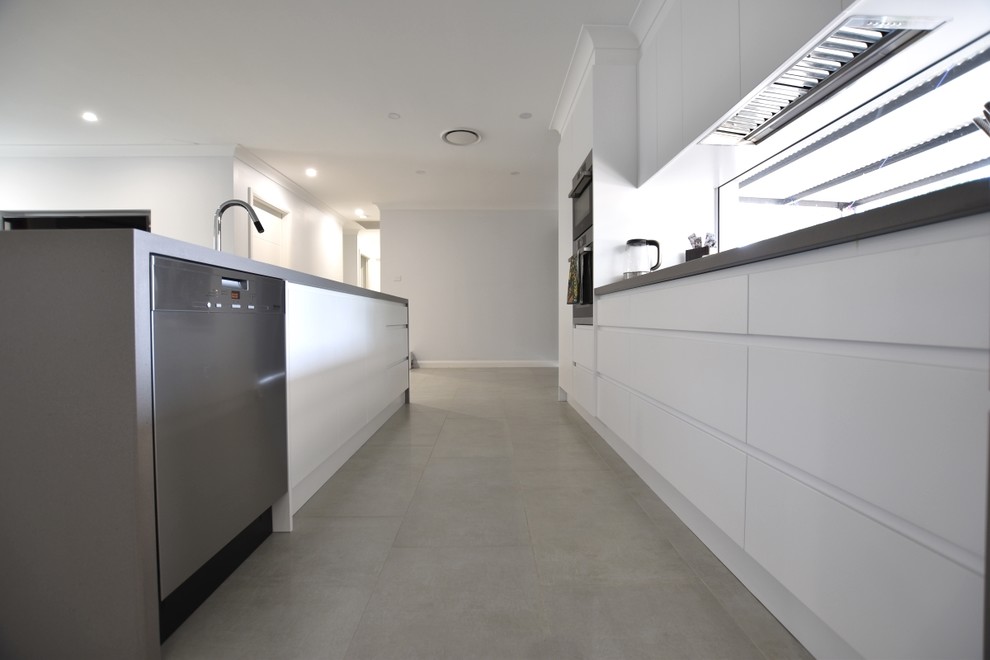 This is an example of a medium sized contemporary single-wall kitchen pantry in Sydney with a built-in sink, flat-panel cabinets, white cabinets, engineered stone countertops, stainless steel appliances, ceramic flooring and an island.