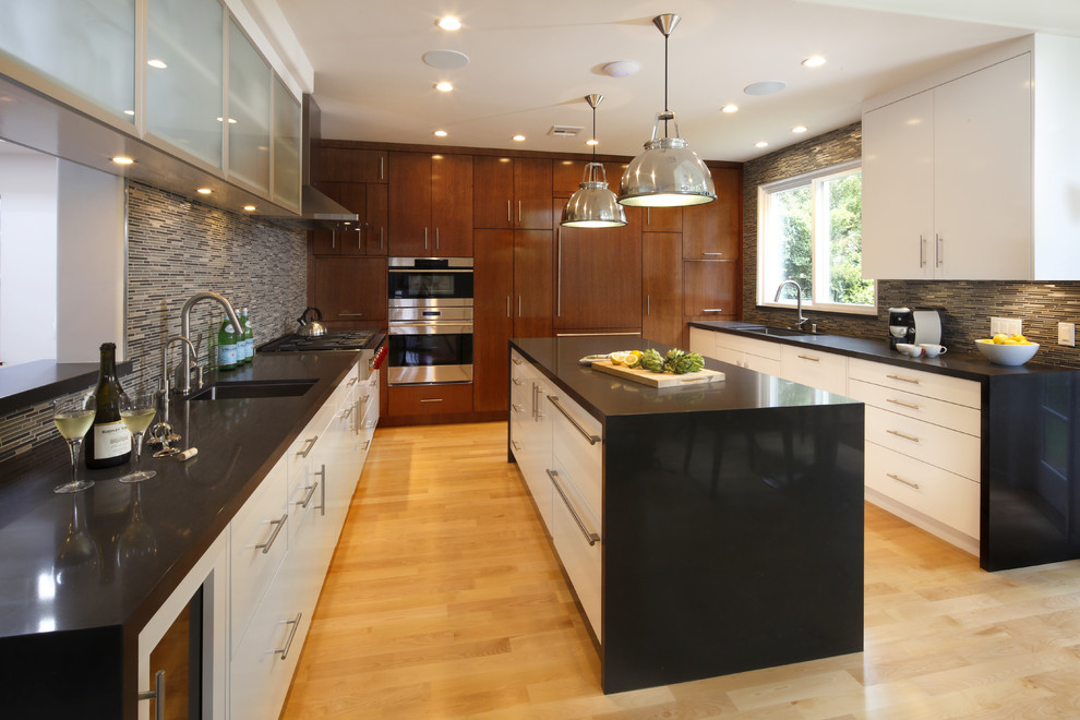Enclosed kitchen - large contemporary u-shaped light wood floor enclosed kitchen idea in Los Angeles with an undermount sink, flat-panel cabinets, white cabinets, solid surface countertops, gray backsplash, matchstick tile backsplash, stainless steel appliances and an island