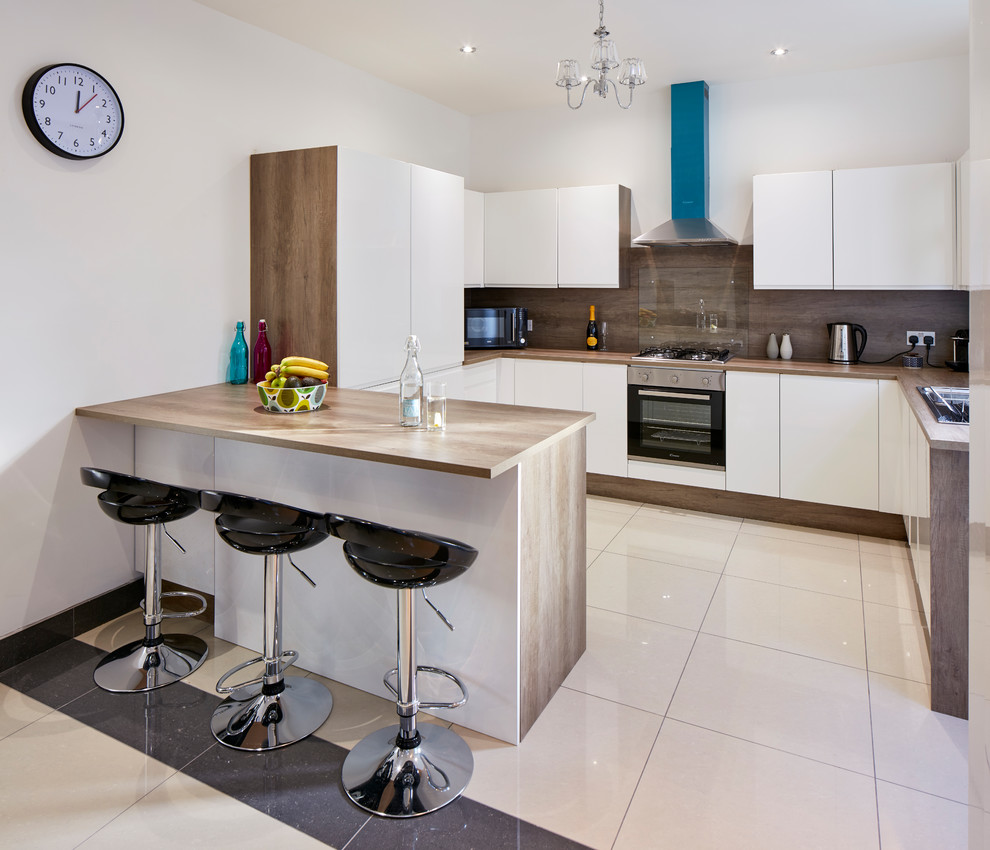 Contemporary l-shaped enclosed kitchen in Cardiff with flat-panel cabinets, white cabinets, wood worktops, brown splashback, black appliances and a breakfast bar.