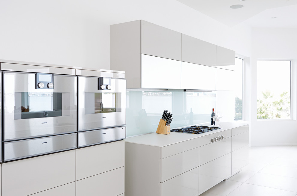 Immagine di un'ampia cucina moderna con lavello a doppia vasca, ante lisce, paraspruzzi bianco, paraspruzzi con lastra di vetro, elettrodomestici in acciaio inossidabile e pavimento in gres porcellanato