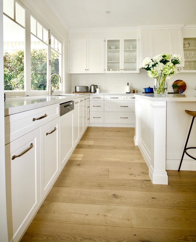 Example of a large transitional u-shaped medium tone wood floor eat-in kitchen design in Sydney with an undermount sink, shaker cabinets, white cabinets, quartz countertops, white backsplash, ceramic backsplash, stainless steel appliances and an island
