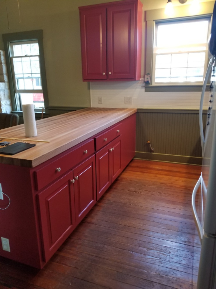 Photo of a small farmhouse u-shaped kitchen/diner in Austin with a belfast sink, raised-panel cabinets, red cabinets, wood worktops, grey splashback, wood splashback, white appliances, medium hardwood flooring, a breakfast bar, brown floors and brown worktops.