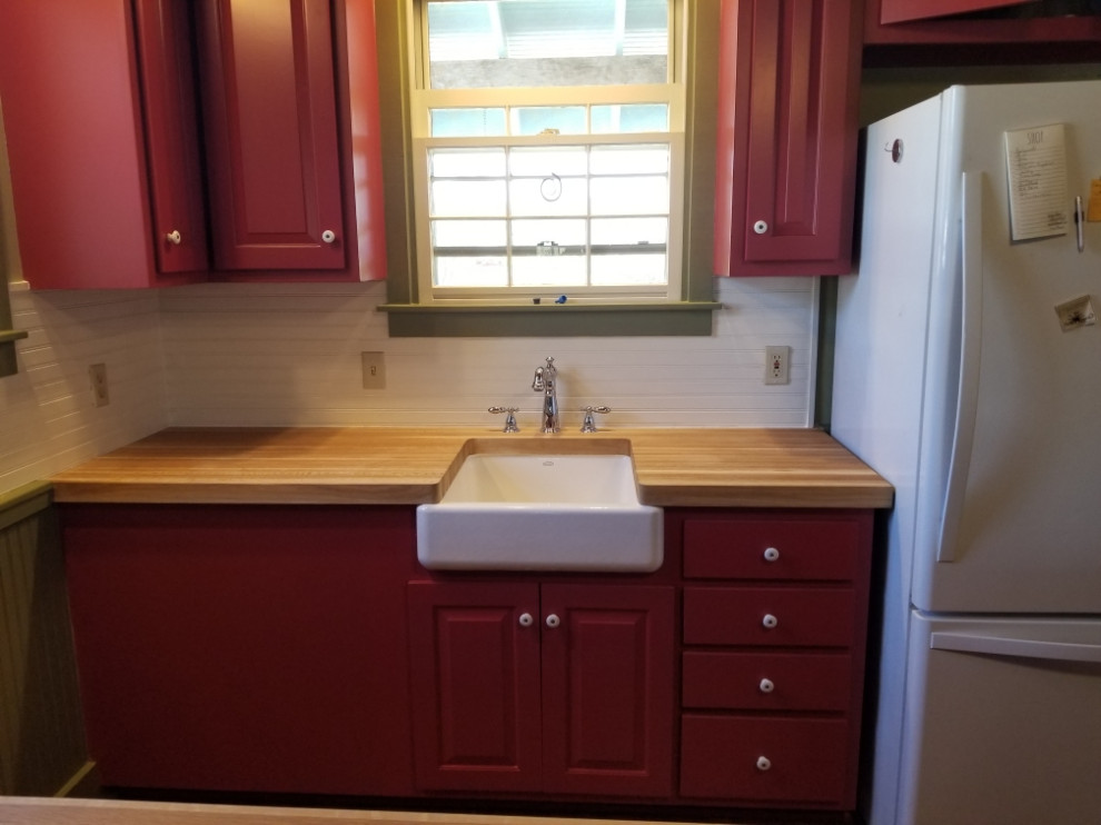 Example of a small cottage u-shaped medium tone wood floor and brown floor eat-in kitchen design in Austin with a farmhouse sink, raised-panel cabinets, red cabinets, wood countertops, gray backsplash, wood backsplash, white appliances, a peninsula and brown countertops