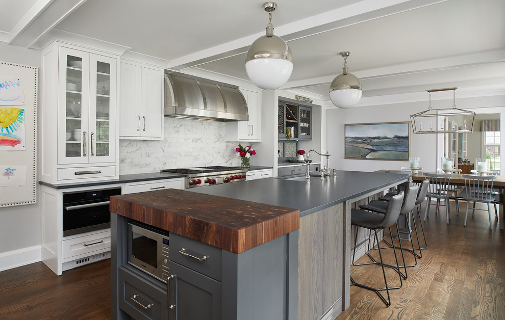 Photo of a traditional single-wall kitchen/diner in Grand Rapids with a submerged sink, white cabinets, white splashback, stainless steel appliances, dark hardwood flooring, an island, black worktops and shaker cabinets.