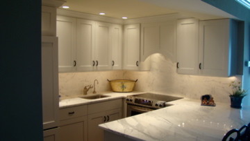 Photo of a beach style u-shaped kitchen/diner in Philadelphia with a submerged sink, recessed-panel cabinets, white cabinets, marble worktops, white splashback, stone slab splashback and integrated appliances.
