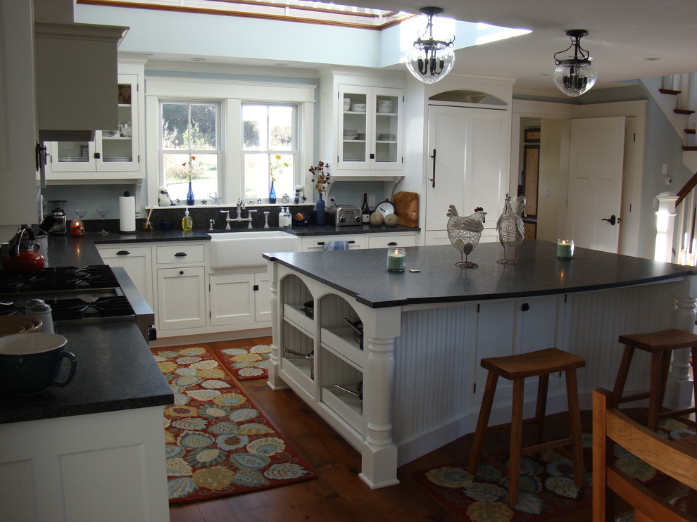 Example of a mid-sized classic l-shaped medium tone wood floor open concept kitchen design in Portland Maine with a farmhouse sink, beaded inset cabinets, white cabinets, granite countertops, black backsplash, stone slab backsplash, paneled appliances and two islands