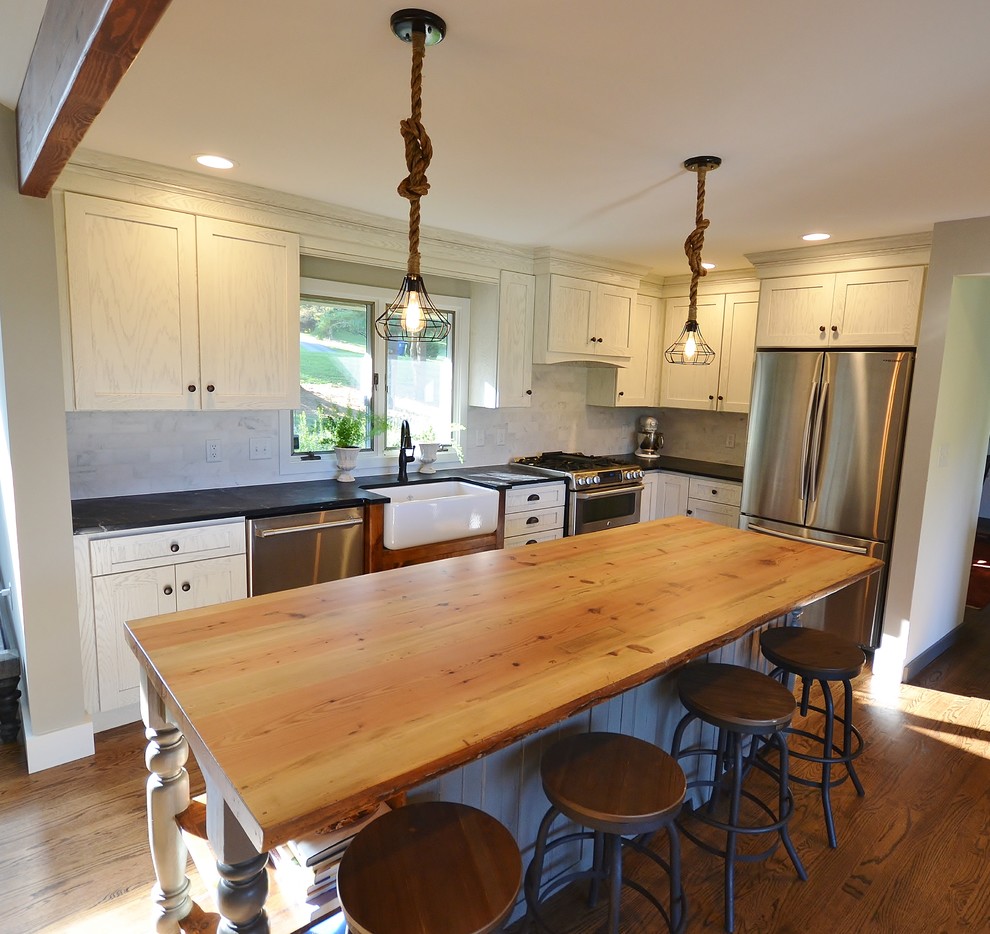 Eat-in kitchen - large rustic l-shaped light wood floor and brown floor eat-in kitchen idea in Philadelphia with a farmhouse sink, recessed-panel cabinets, white cabinets, wood countertops, white backsplash, subway tile backsplash, stainless steel appliances, an island and brown countertops