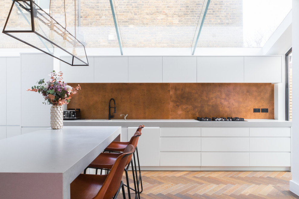 Einzeilige Moderne Wohnküche mit flächenbündigen Schrankfronten, weißen Schränken, hellem Holzboden, Kücheninsel und Küchenrückwand in Metallic in London