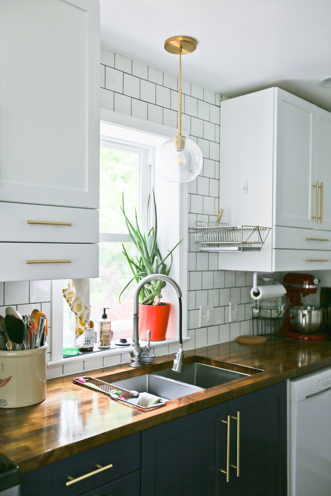 Cette photo montre une petite cuisine américaine parallèle rétro avec un placard avec porte à panneau encastré, des portes de placard bleues, un plan de travail en bois, une crédence blanche, un sol en bois brun et un plan de travail marron.