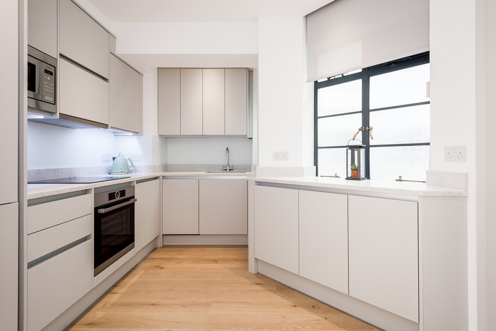 Foto di una piccola cucina minimalista con ante bianche, top in quarzite, elettrodomestici in acciaio inossidabile, parquet chiaro e top bianco