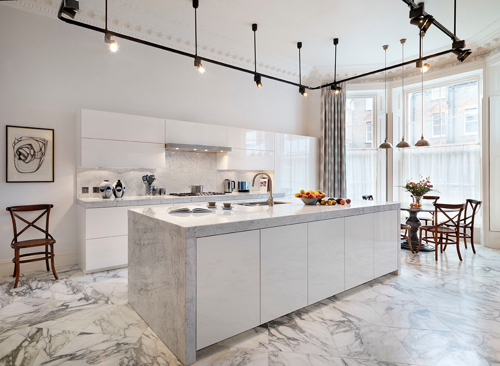This is an example of an expansive contemporary galley open plan kitchen in London with a belfast sink, flat-panel cabinets, white cabinets, marble worktops, white splashback, stone slab splashback, integrated appliances, marble flooring and an island.