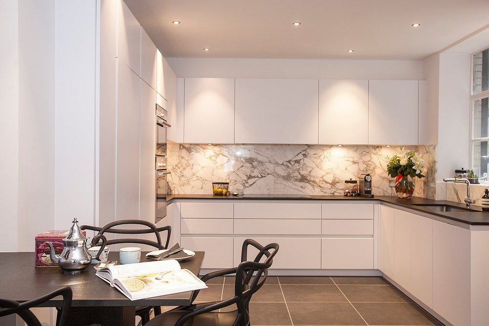 Example of a mid-sized trendy u-shaped porcelain tile and black floor enclosed kitchen design in London with an undermount sink, flat-panel cabinets, white cabinets, granite countertops, marble backsplash, paneled appliances, no island and black countertops