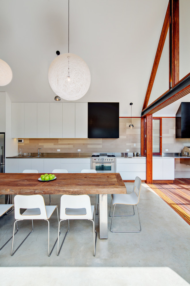 Example of a mid-sized trendy single-wall concrete floor open concept kitchen design in Other with flat-panel cabinets, white cabinets, stainless steel countertops, stainless steel appliances and an integrated sink