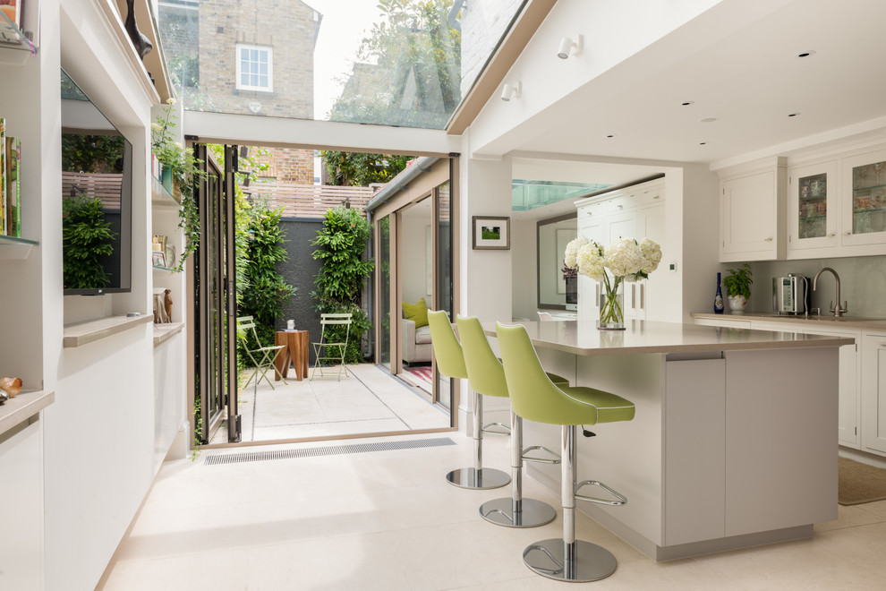 This is an example of a large contemporary l-shaped open plan kitchen in London with a double-bowl sink, raised-panel cabinets, distressed cabinets, composite countertops, beige splashback, glass tiled splashback, stainless steel appliances, limestone flooring and an island.