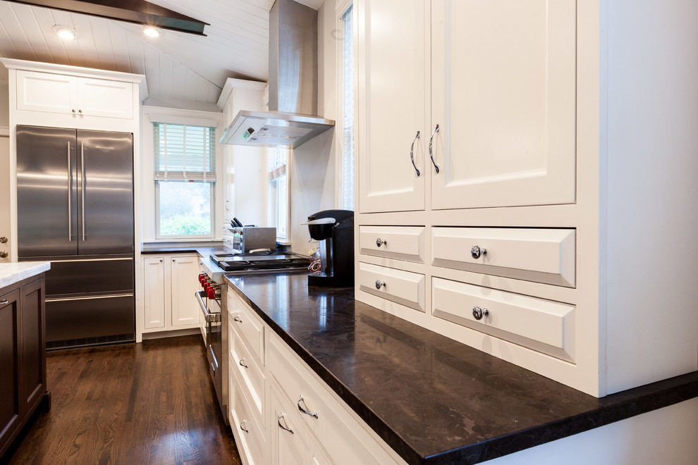 This is an example of a large traditional l-shaped kitchen/diner in Chicago with a submerged sink, recessed-panel cabinets, white cabinets, quartz worktops, stainless steel appliances, medium hardwood flooring, an island and brown floors.