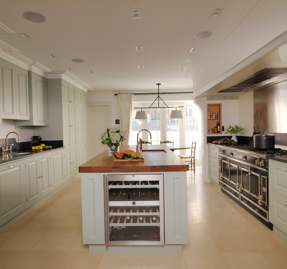 This is an example of a medium sized classic galley kitchen/diner in Other with raised-panel cabinets, green cabinets, an integrated sink, granite worktops, stainless steel appliances, limestone flooring, an island, beige floors and black worktops.