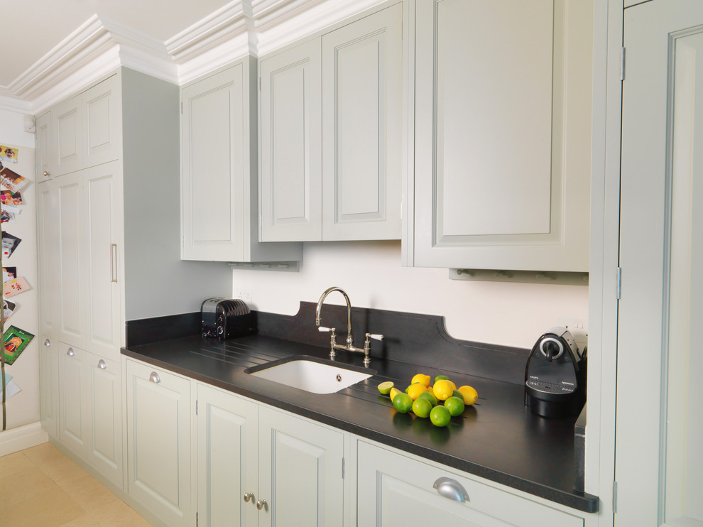 This is an example of a medium sized contemporary galley kitchen/diner in Other with an integrated sink, raised-panel cabinets, green cabinets, granite worktops, stainless steel appliances, limestone flooring, an island, white floors and black worktops.