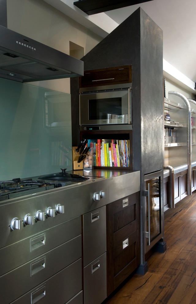 Foto de cocina actual grande con encimera de acero inoxidable, salpicadero verde, salpicadero de vidrio templado y suelo de madera oscura