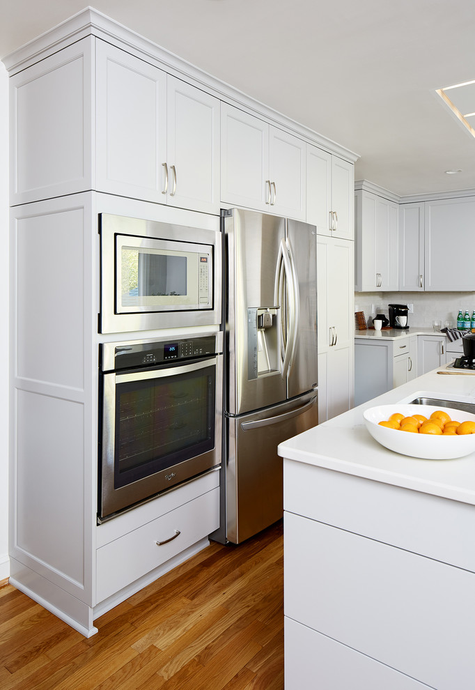 Große Klassische Wohnküche in L-Form mit weißen Schränken, Küchenrückwand in Weiß, Rückwand aus Metrofliesen, Küchengeräten aus Edelstahl, braunem Holzboden und Kücheninsel in Washington, D.C.
