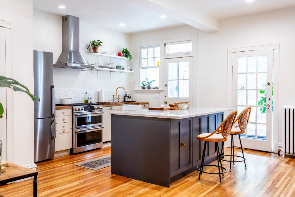Inspiration for a large country single-wall medium tone wood floor eat-in kitchen remodel in Richmond with a farmhouse sink, shaker cabinets, beige cabinets, wood countertops, white backsplash, subway tile backsplash, stainless steel appliances and an island