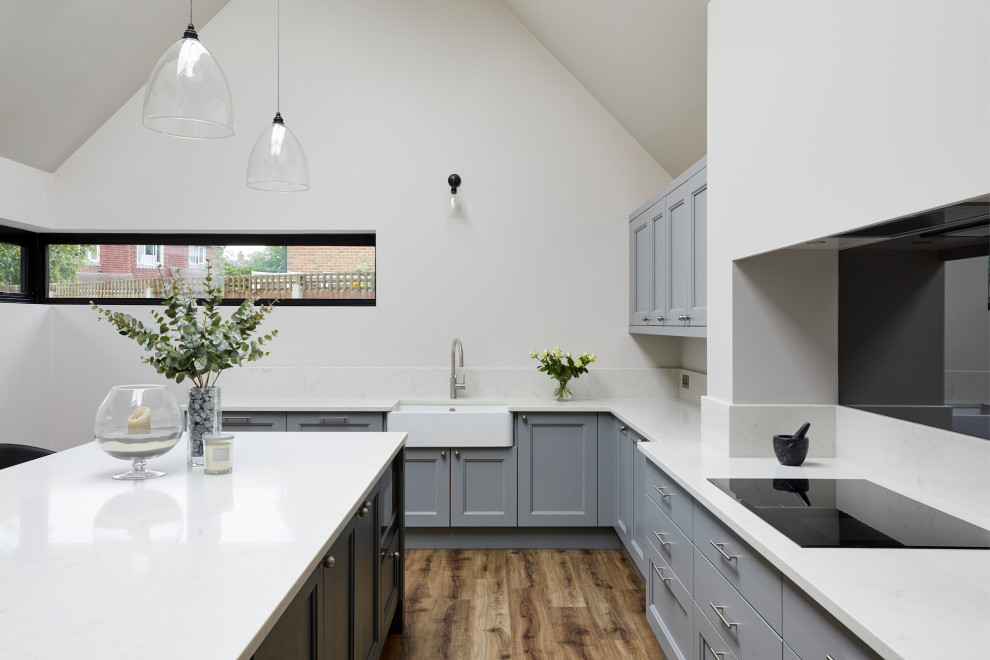 Design ideas for a large farmhouse u-shaped open plan kitchen in Kent with a belfast sink, shaker cabinets, grey cabinets, quartz worktops, mirror splashback, stainless steel appliances, medium hardwood flooring, an island, brown floors, white worktops and a vaulted ceiling.