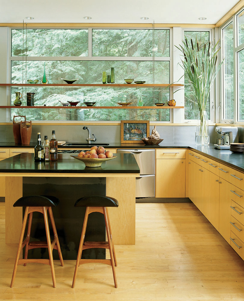 This is an example of a contemporary l-shaped kitchen in New York with flat-panel cabinets, light wood cabinets, window splashback, stainless steel appliances, light hardwood flooring, an island, beige floors and black worktops.