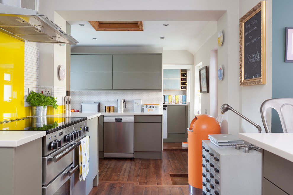 Photo of a medium sized bohemian enclosed kitchen in Kent with laminate floors, brown floors, grey cabinets, yellow splashback, glass sheet splashback, stainless steel appliances, no island and white worktops.