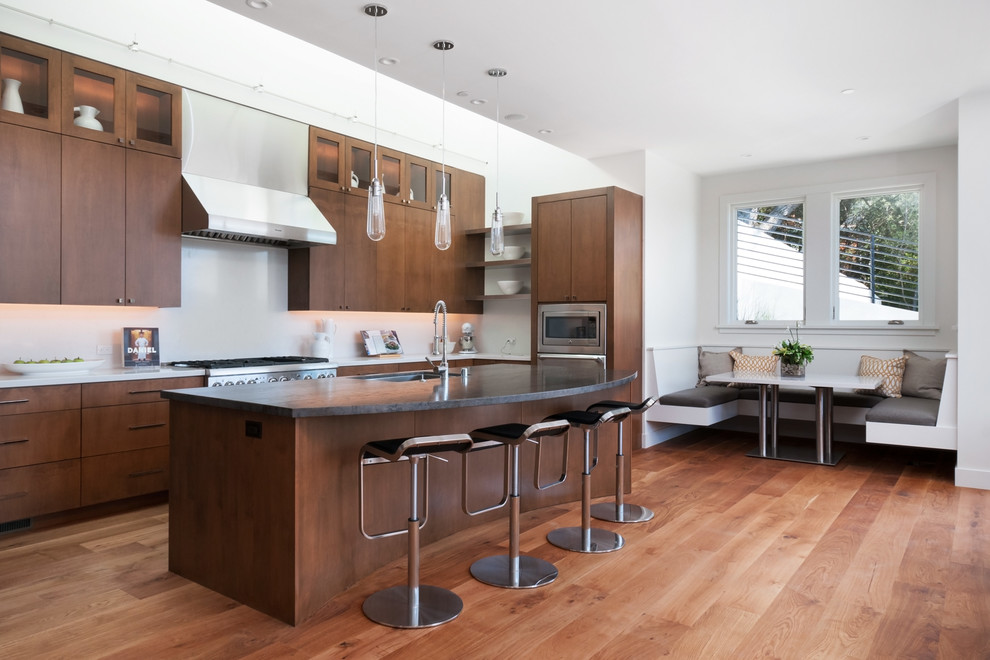 Example of a trendy l-shaped medium tone wood floor eat-in kitchen design in San Francisco with an undermount sink, flat-panel cabinets, dark wood cabinets, white backsplash, stainless steel appliances and an island