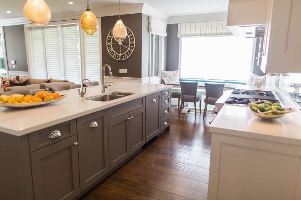 Example of a large transitional l-shaped medium tone wood floor open concept kitchen design in San Francisco with an undermount sink, shaker cabinets, solid surface countertops, mirror backsplash, stainless steel appliances, an island and gray cabinets