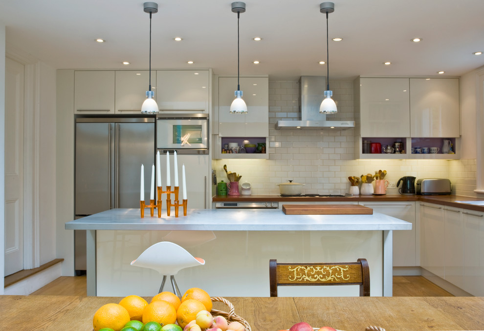 Design ideas for a contemporary kitchen in London with an island, flat-panel cabinets, stainless steel worktops, stainless steel appliances and light hardwood flooring.