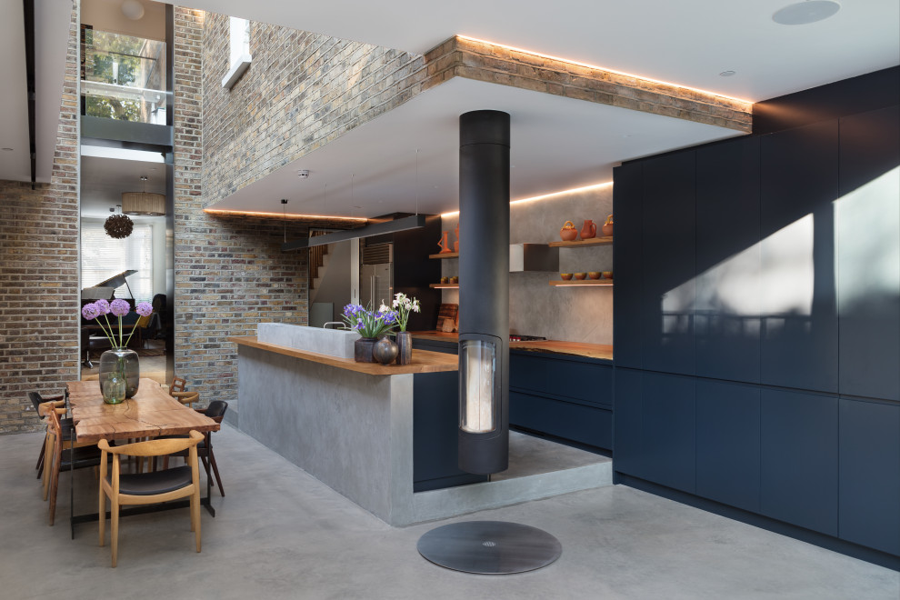 Modern inredning av ett stort brun brunt kök, med en nedsänkt diskho, släta luckor, blå skåp, träbänkskiva, grått stänkskydd, integrerade vitvaror, betonggolv, en köksö och grått golv