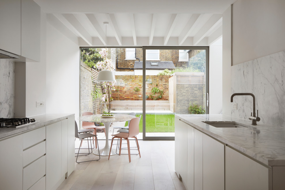 Contemporary galley kitchen/diner in London with a submerged sink, flat-panel cabinets, white cabinets, grey splashback, stone slab splashback, light hardwood flooring, no island, beige floors, grey worktops and exposed beams.