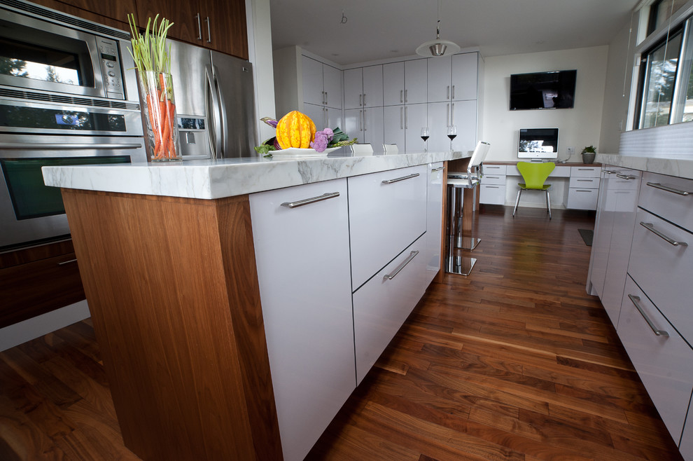 Eat-in kitchen - mid-sized contemporary u-shaped medium tone wood floor and brown floor eat-in kitchen idea in Vancouver with an undermount sink, flat-panel cabinets, white cabinets, marble countertops, white backsplash, subway tile backsplash, stainless steel appliances and an island