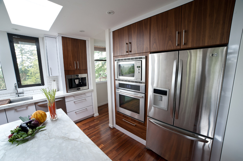 Photo of a medium sized contemporary u-shaped kitchen/diner in Vancouver with a submerged sink, flat-panel cabinets, marble worktops, white splashback, metro tiled splashback, stainless steel appliances, medium hardwood flooring, an island, white cabinets and brown floors.