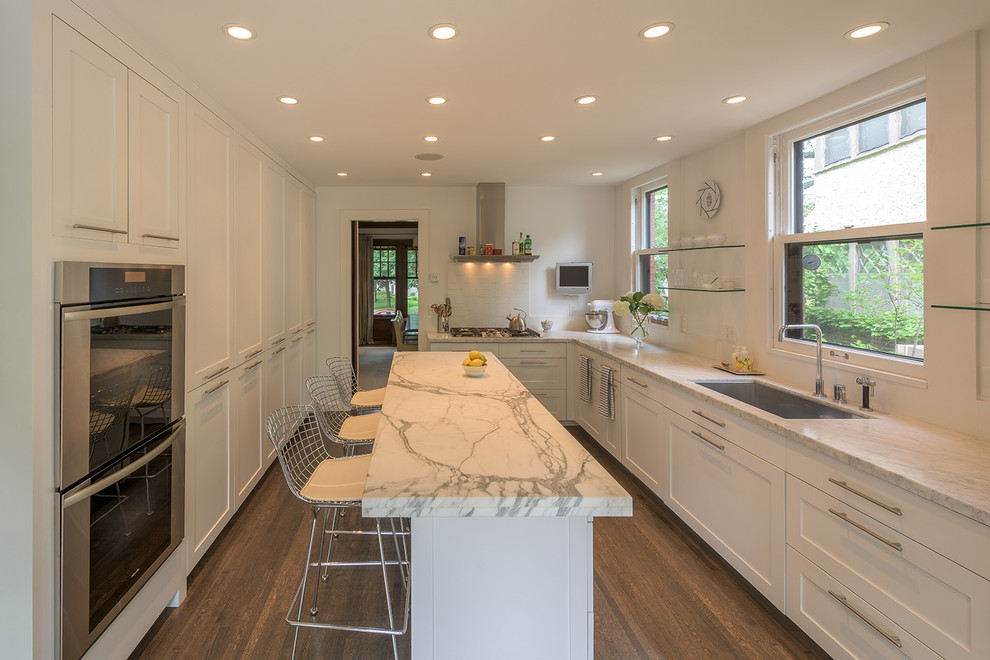 Example of a large transitional u-shaped dark wood floor enclosed kitchen design in Minneapolis with an undermount sink, shaker cabinets, white cabinets, marble countertops, white backsplash, porcelain backsplash, stainless steel appliances and an island