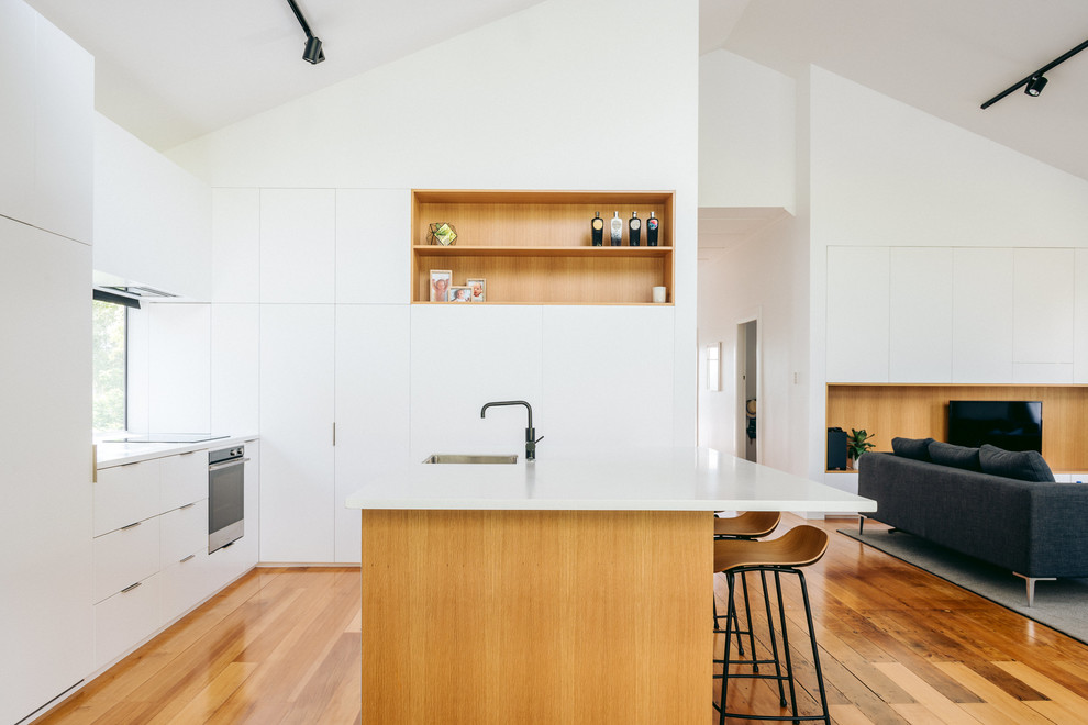 Inspiration for a contemporary kitchen in Auckland with a submerged sink, flat-panel cabinets, white cabinets, glass sheet splashback, integrated appliances and an island.