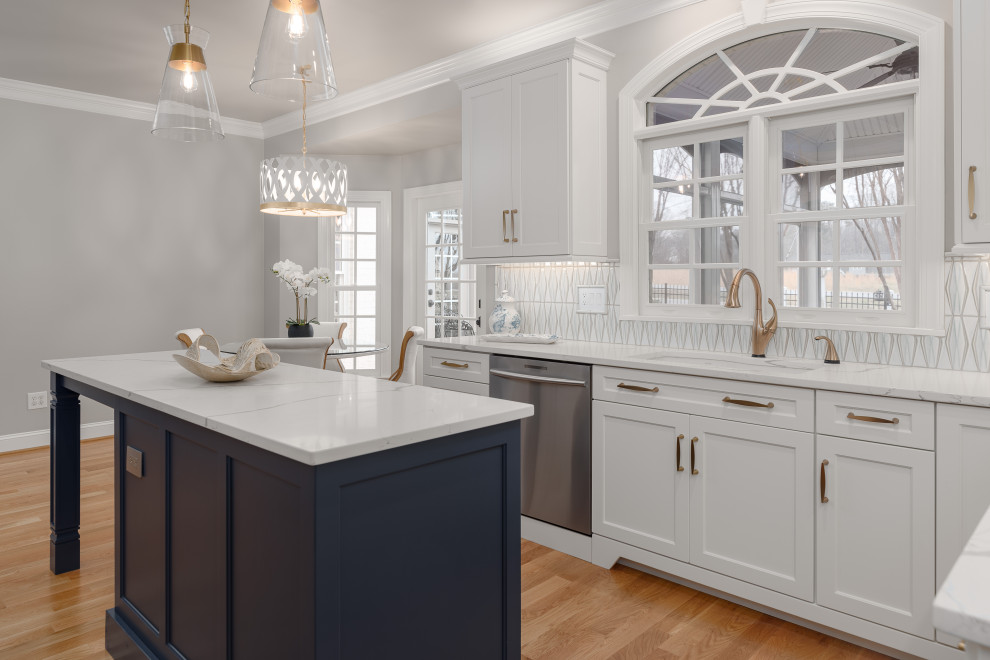 Klassisk inredning av ett stort vit vitt kök, med en undermonterad diskho, luckor med infälld panel, vita skåp, bänkskiva i kvarts, vitt stänkskydd, stänkskydd i keramik, rostfria vitvaror, mellanmörkt trägolv, en köksö och brunt golv