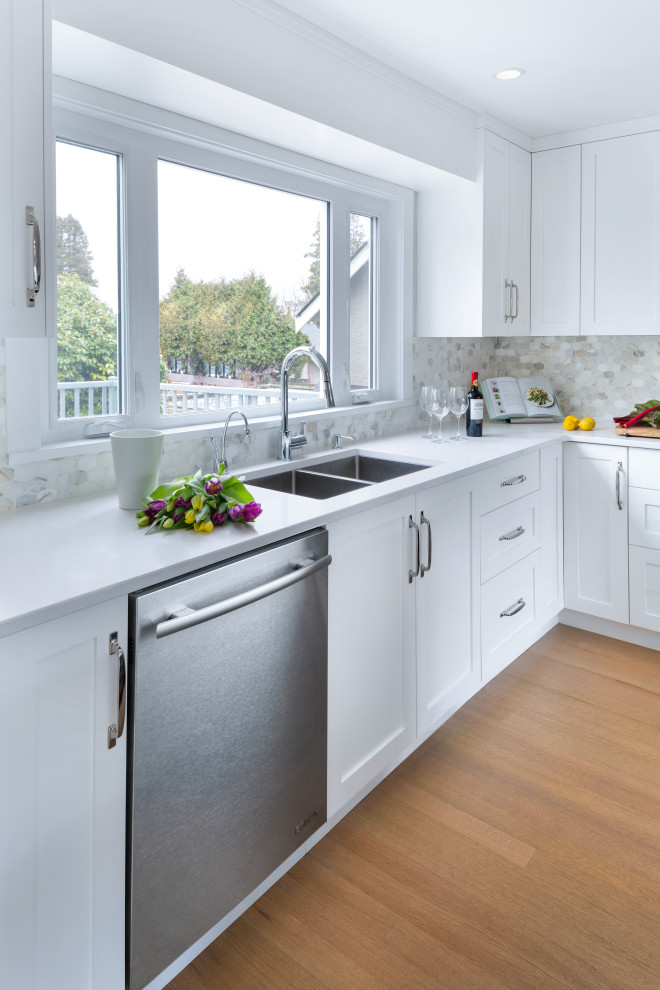 Example of a large trendy l-shaped brown floor eat-in kitchen design in Vancouver with an undermount sink, shaker cabinets, white cabinets, quartzite countertops, beige backsplash, mosaic tile backsplash, stainless steel appliances, an island and white countertops